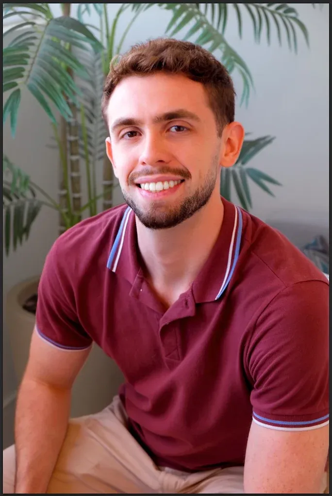 Gabriel Bauer sorrindo, de camisa polo vinho, com plantas ao fundo
