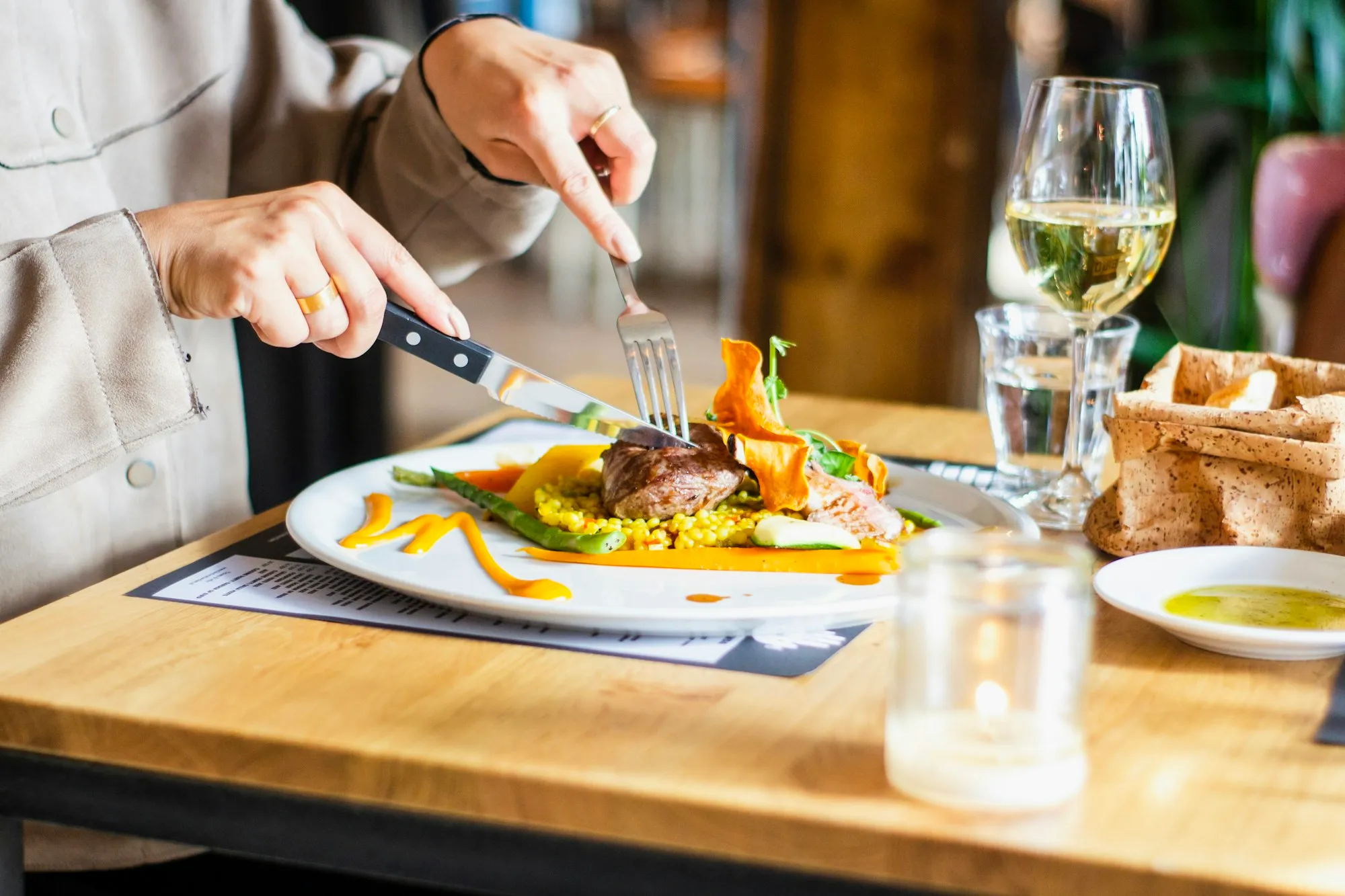 Pessoa cortando um prato num restaurante, com taças sobre a mesa
